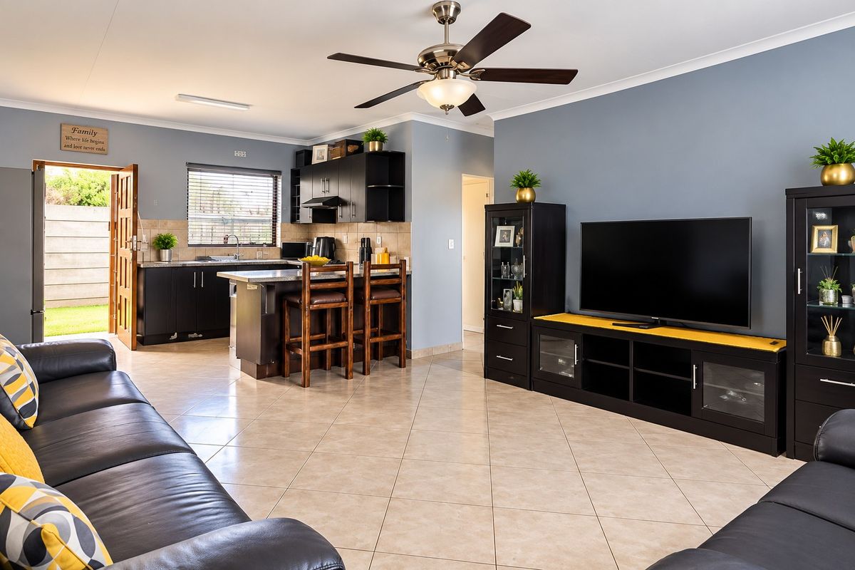 Spacious open-plan living area featuring a modern kitchen with dark cabinetry, a central island, and tiled flooring throughout, seamlessly connecting to the living space.