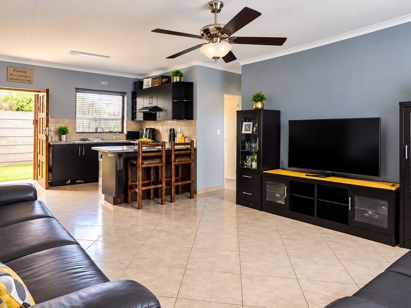 Spacious open-plan living area featuring a modern kitchen with dark cabinetry, a central island, and tiled flooring throughout, seamlessly connecting to the living space.