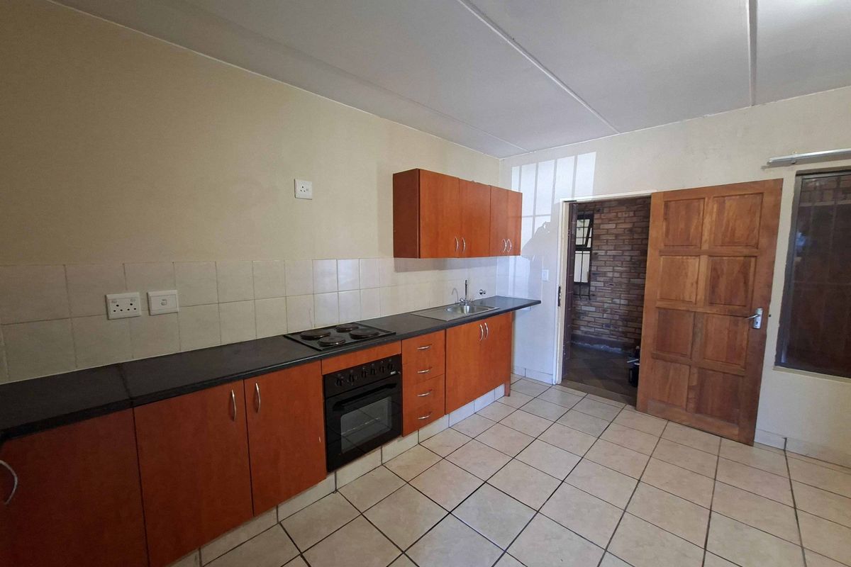 A functional kitchen featuring wooden cabinetry, a built-in oven and hob, tiled flooring, and a tiled backsplash, offering a clean and practical workspace.
