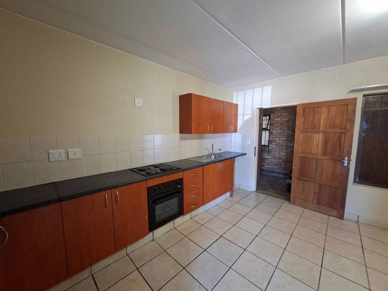 A functional kitchen featuring wooden cabinetry, a built-in oven and hob, tiled flooring, and a tiled backsplash, offering a clean and practical workspace.