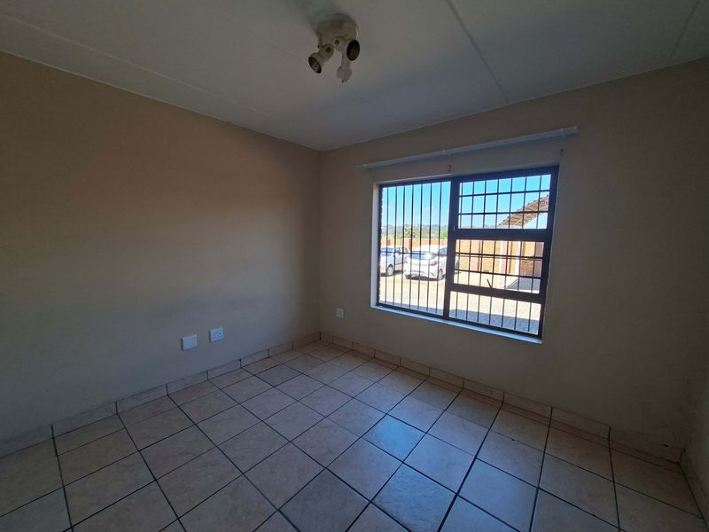 A vacant bedroom featuring neutral tiled flooring, a window with security bars, and a ceiling-mounted light fixture.