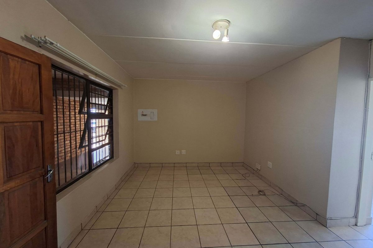 An empty living area featuring tiled flooring, security bars on the window, and a central ceiling light fixture.