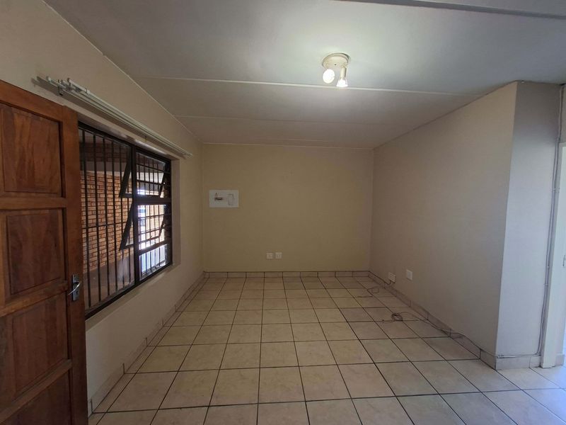 An empty living area featuring tiled flooring, security bars on the window, and a central ceiling light fixture.
