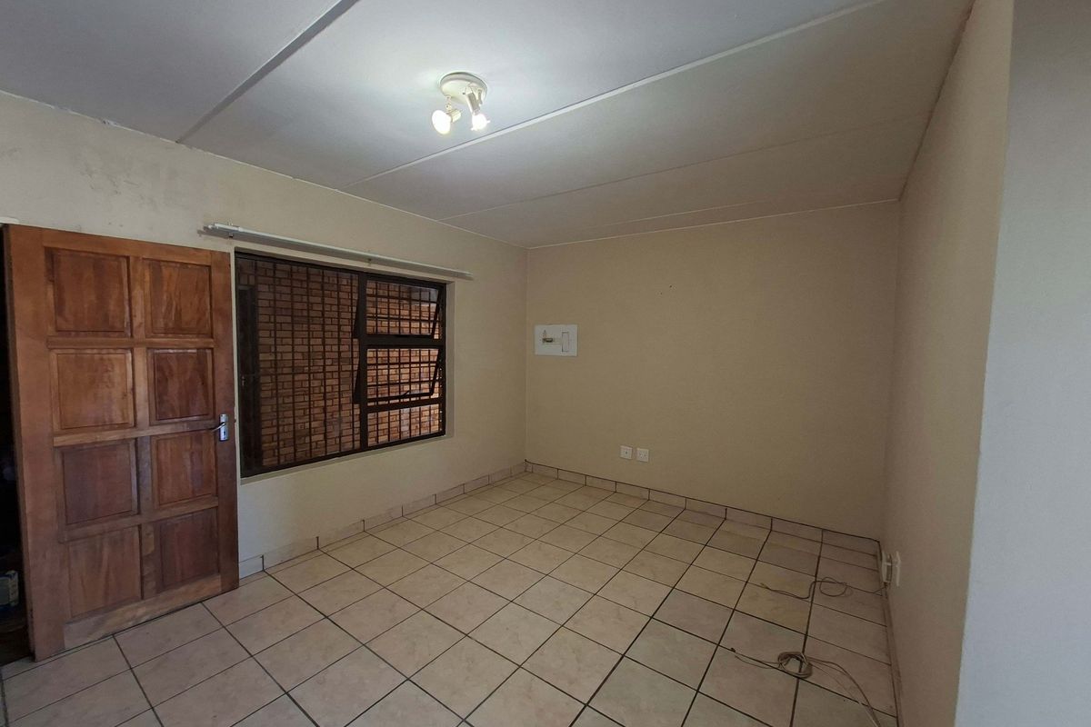 An empty bedroom featuring tiled flooring, a wooden door, and security burglar bars on the window. The space requires minor cosmetic updates.