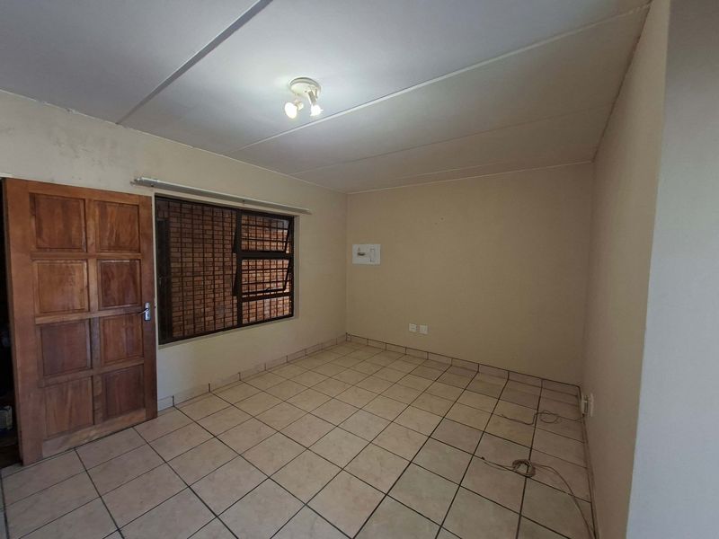 An empty bedroom featuring tiled flooring, a wooden door, and security burglar bars on the window. The space requires minor cosmetic updates.