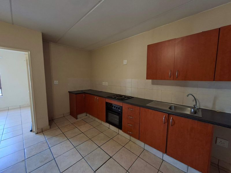 A functional kitchen featuring laminate cabinetry, a built-in oven with electric hob, stainless steel sink, and tiled flooring.