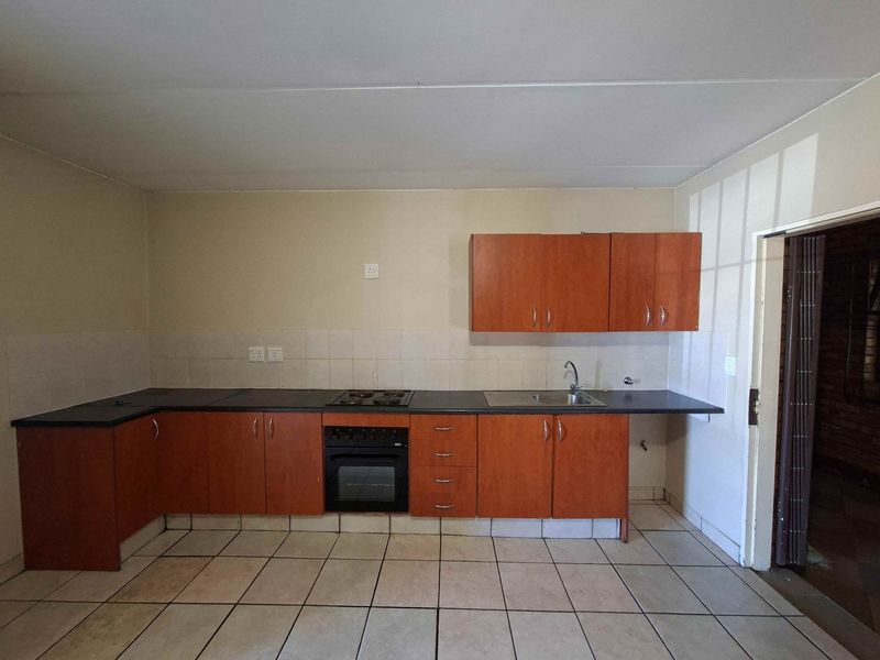 A functional kitchen featuring built-in wooden cabinetry, a hob, an oven, and a stainless steel sink with tiled flooring and backsplash.