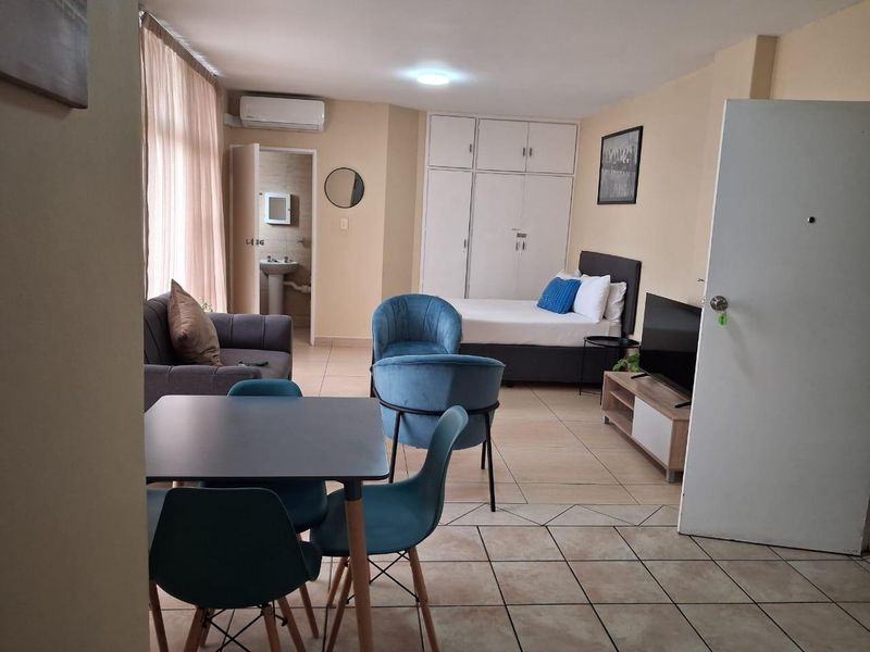 Open-plan studio apartment featuring tiled flooring, built-in storage cupboards, an air conditioning unit, and an en-suite bathroom with a pedestal sink.