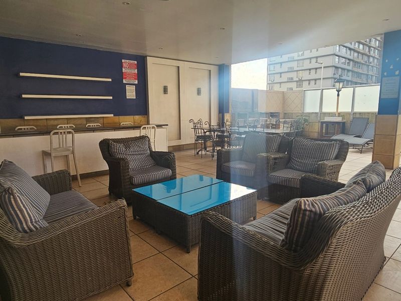 Spacious covered patio area featuring a built-in bar counter, tiled flooring, and glass balustrades, ideal for outdoor entertaining.