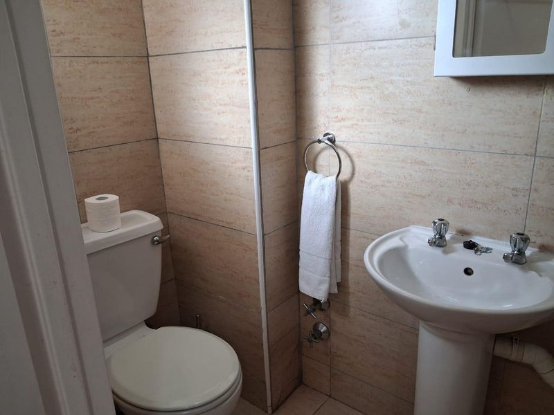 A compact bathroom featuring tiled walls, a pedestal basin, and a standard toilet, offering a functional layout with basic fixtures.