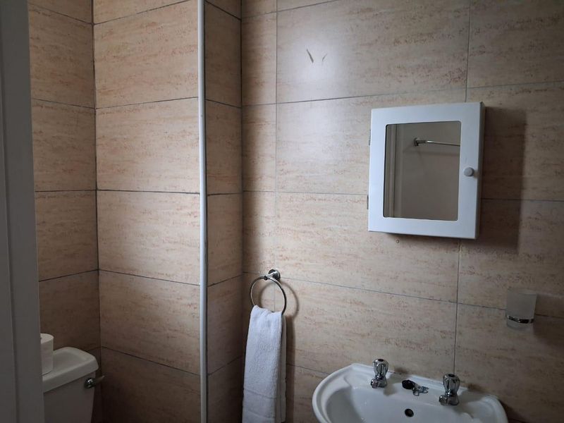 A functional bathroom featuring tiled walls, a wall-mounted medicine cabinet, a ceramic washbasin, and a standard toilet.