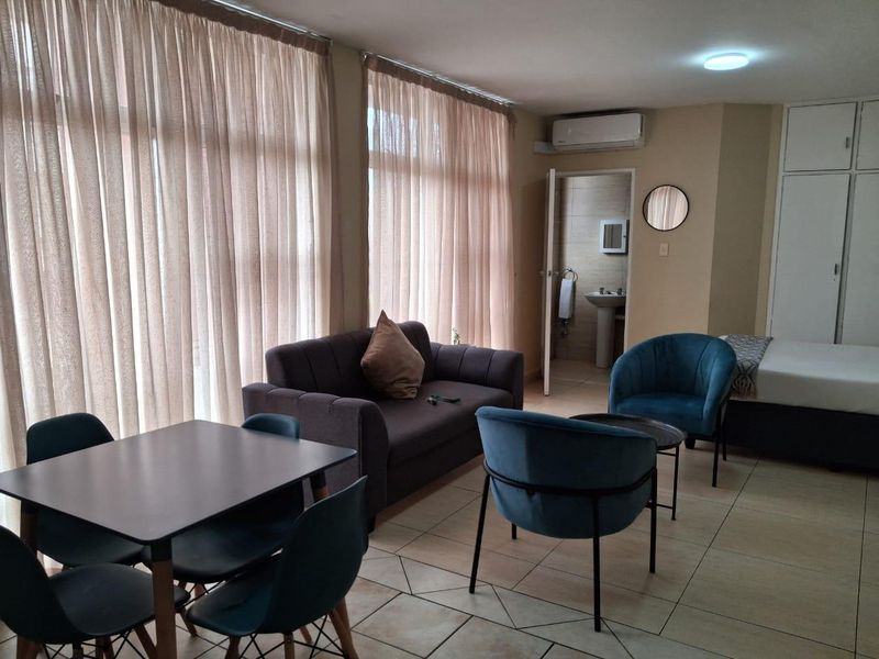 Open-plan living area featuring tiled flooring, built-in cupboards, and an air conditioning unit, with direct access to an en-suite bathroom.