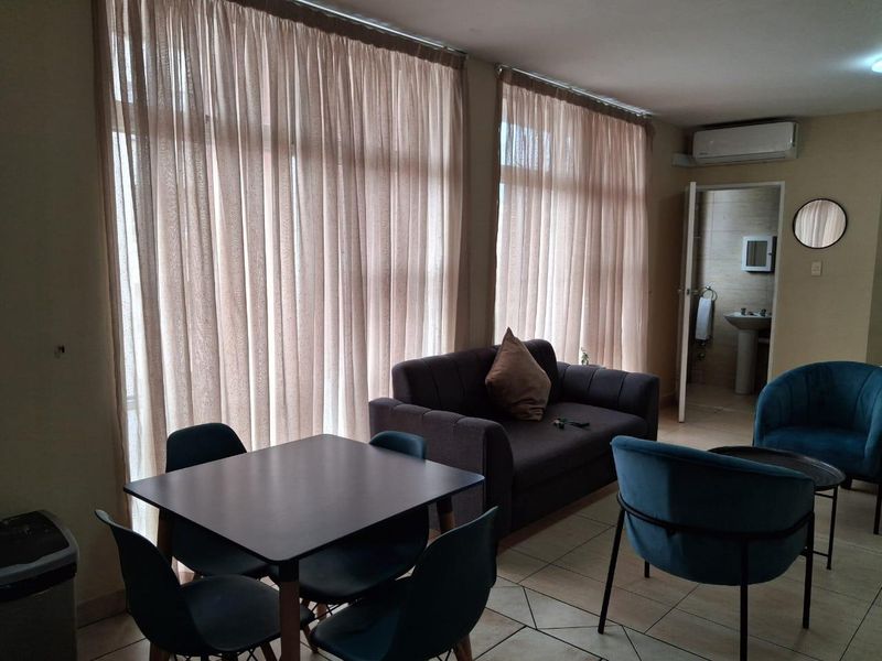 Open-plan living area featuring tiled flooring, large windows with natural light, and a wall-mounted air conditioning unit.