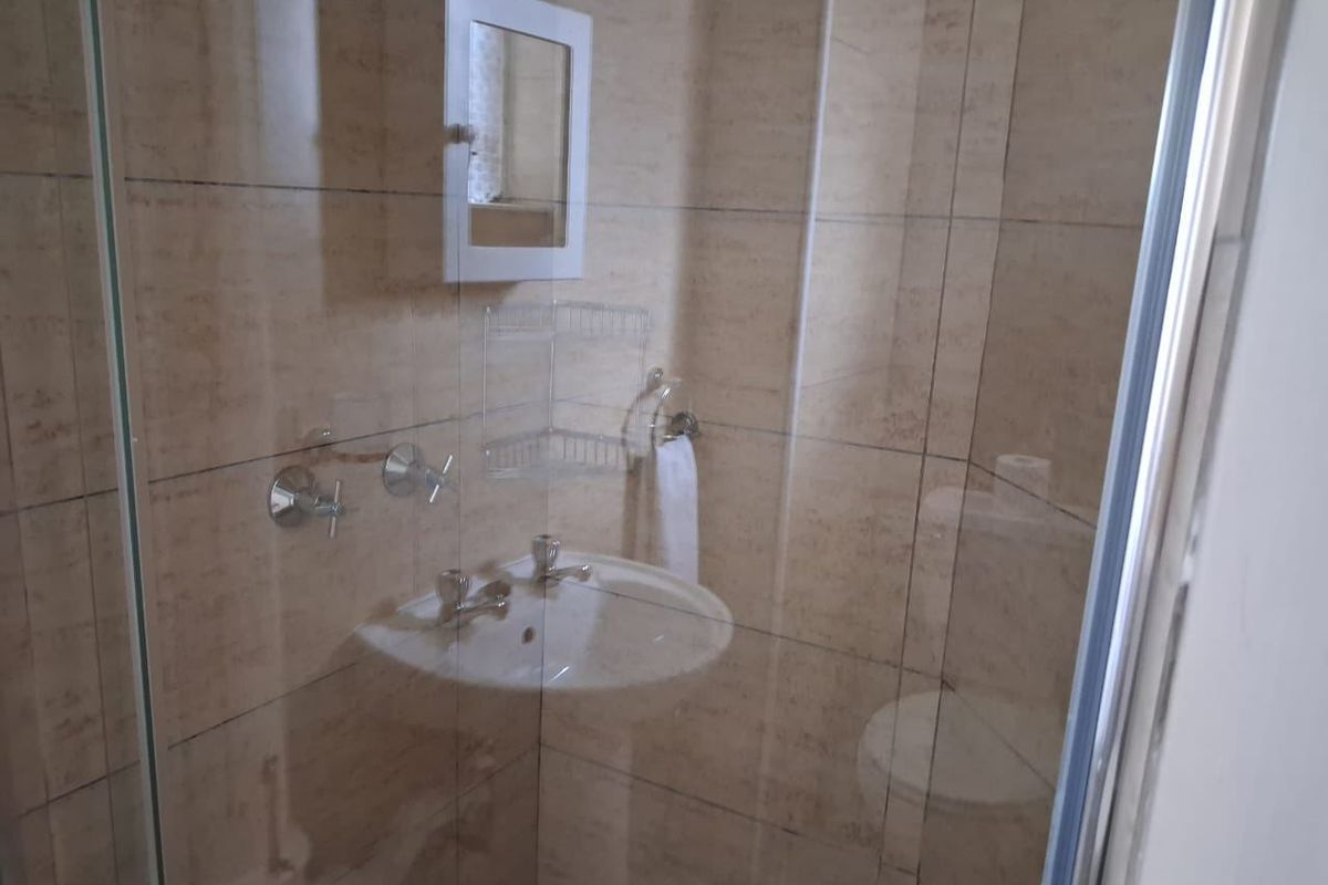 A compact bathroom featuring a wall-mounted basin, chrome fixtures, and a glass-enclosed shower area with neutral wall tiling.