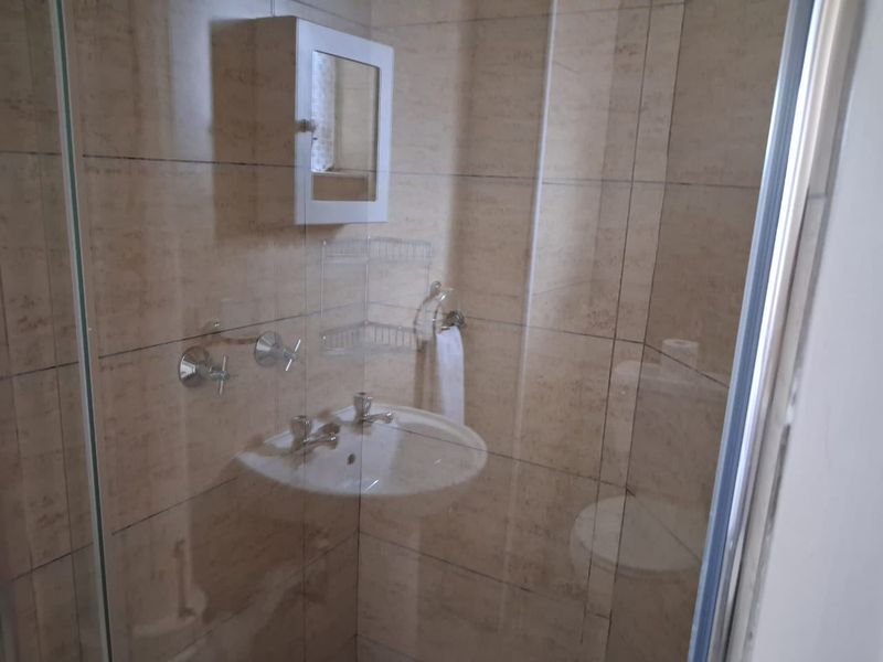 A compact bathroom featuring a wall-mounted basin, chrome fixtures, and a glass-enclosed shower area with neutral wall tiling.