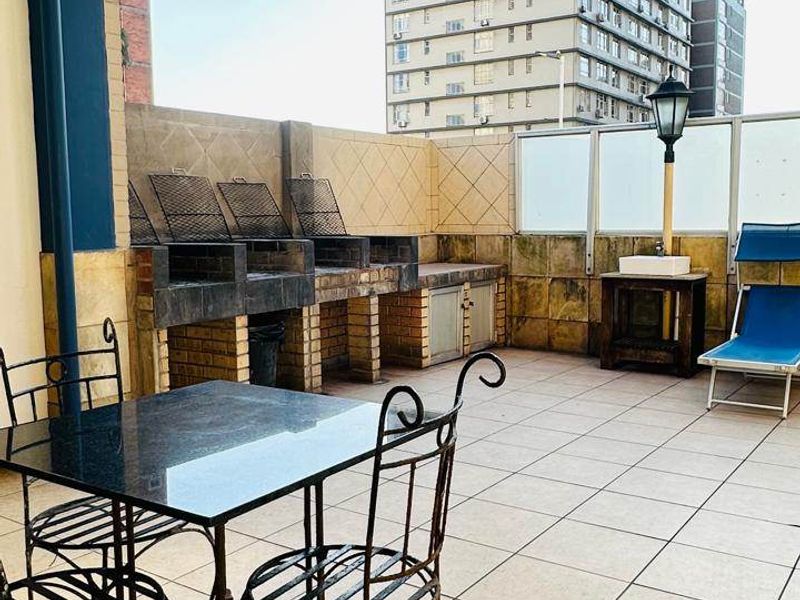 Spacious balcony featuring a built-in brick braai area, tiled flooring, and glass balustrades, offering an ideal space for outdoor entertaining.