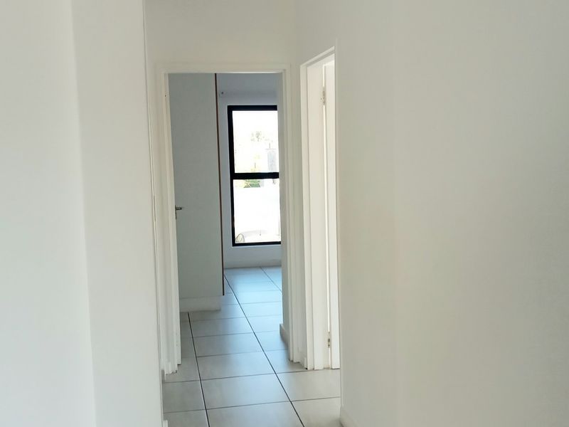 A clean, bright hallway featuring neutral tiled flooring and white walls, providing access to adjacent rooms within the apartment.