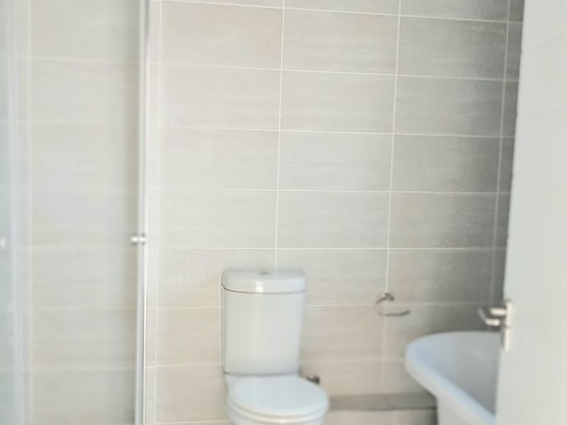 A clean, modern bathroom featuring a glass shower enclosure, a white toilet, and a freestanding bathtub with neutral wall and floor tiling.
