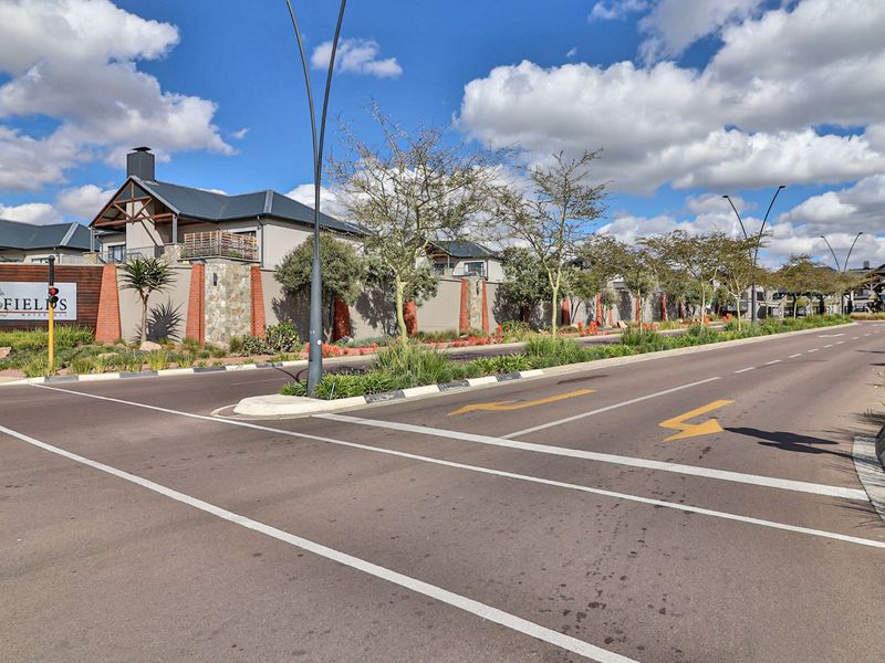 Street view of the Polo Fields estate entrance, featuring well-maintained perimeter walls, stone and brick architectural detailing, and landscaped road verges.