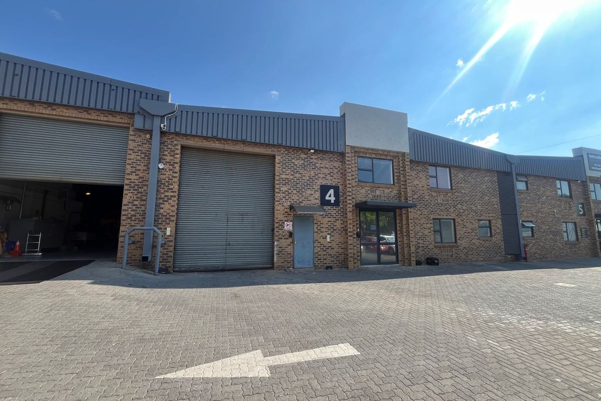 Front elevation of an industrial unit featuring face brick construction, a large roller shutter door, and paved driveway access.