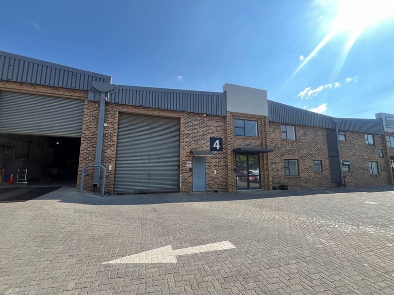 Front elevation of an industrial unit featuring face brick construction, a large roller shutter door, and paved driveway access.