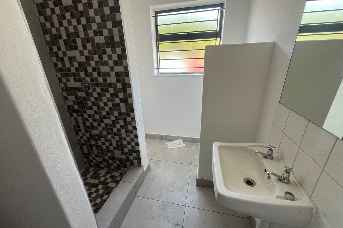 A functional bathroom featuring a tiled shower enclosure, pedestal basin, and neutral floor tiles, offering a clean and practical space.