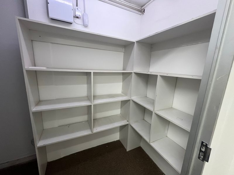 A functional utility storage area featuring built-in corner shelving units and an accessible electrical distribution board.