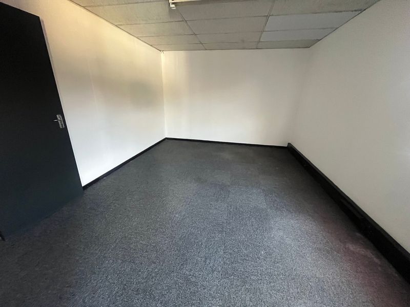 An empty office space featuring grey carpet tiles, a suspended ceiling, and a dark interior door, suitable for a professional workspace.