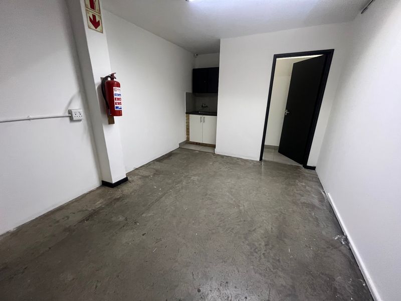 A functional utility space featuring concrete flooring, a small kitchenette area with cabinetry and a sink, and a wall-mounted fire extinguisher.