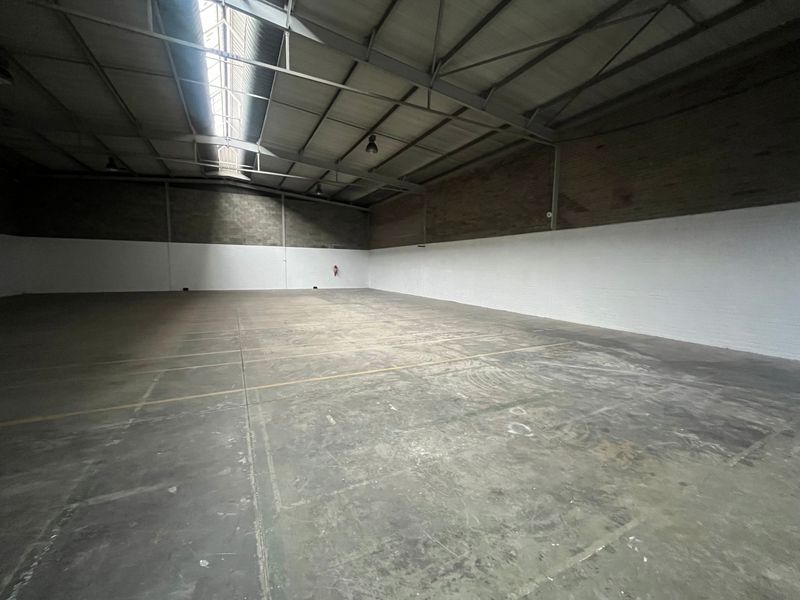 Spacious industrial warehouse unit featuring high ceilings with exposed steel trusses, a central skylight, and durable concrete flooring.