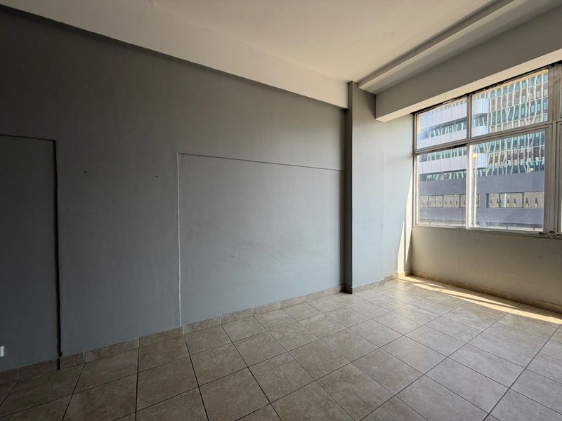 An empty, sunlit living area featuring neutral grey walls and tiled flooring, offering a blank canvas for interior design and personalization.