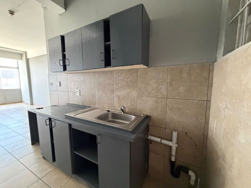 A basic kitchen area featuring dark grey built-in cabinetry, a stainless steel sink, and tiled backsplash, currently in need of cosmetic updates.