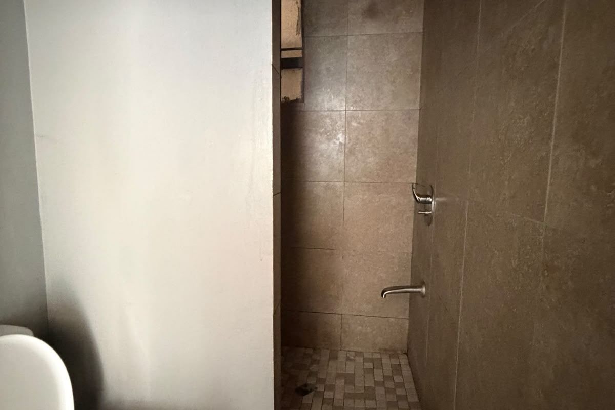 A functional bathroom featuring a tiled shower enclosure and standard toilet, currently in need of cosmetic updates to improve its overall condition.