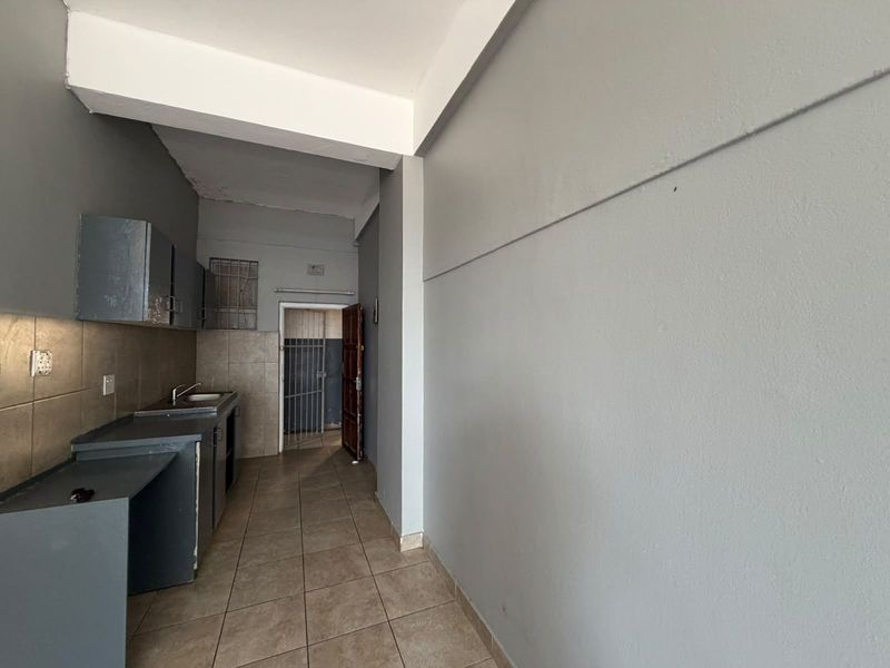 A compact, empty kitchen area featuring built-in cabinetry, tiled flooring, and a tiled backsplash, leading to a secure rear entrance.