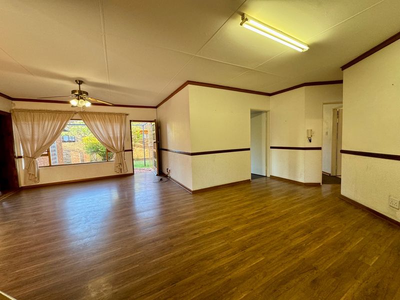 Spacious, empty living area featuring laminate flooring, a ceiling fan, and neutral walls with chair rail molding, offering direct access to the rear garden.