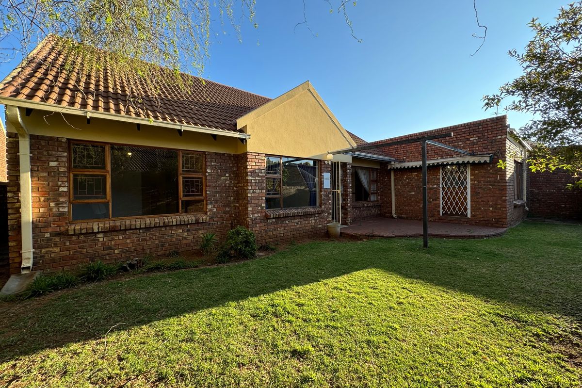 Rear view of the townhouse featuring a brick facade, tiled roof, paved patio area, and a well-maintained lawn.