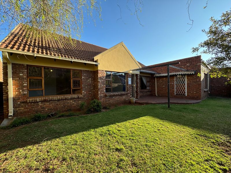 Rear view of the townhouse featuring a brick facade, tiled roof, paved patio area, and a well-maintained lawn.