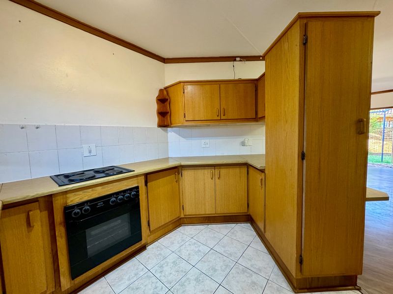 A functional kitchen featuring wooden cabinetry, laminate countertops, a built-in oven and hob, and tiled flooring, offering a classic layout ready for modernization.