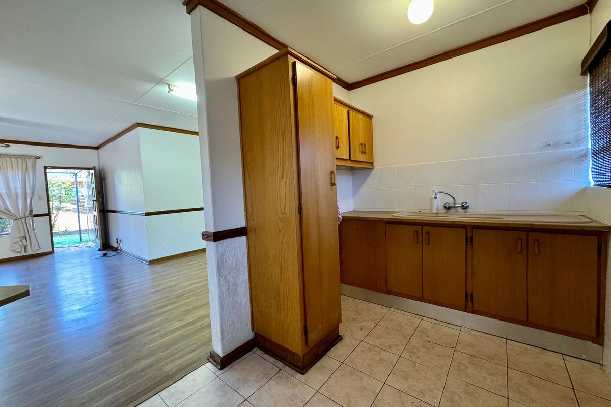 A dated kitchen area featuring wooden cabinetry, tiled flooring, and a sink, adjacent to an open-plan living space with laminate flooring.
