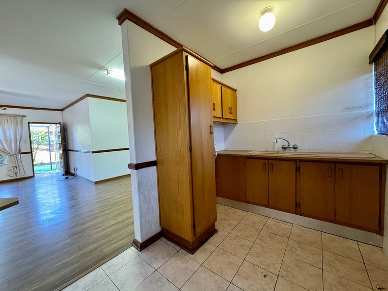 A dated kitchen area featuring wooden cabinetry, tiled flooring, and a sink, adjacent to an open-plan living space with laminate flooring.