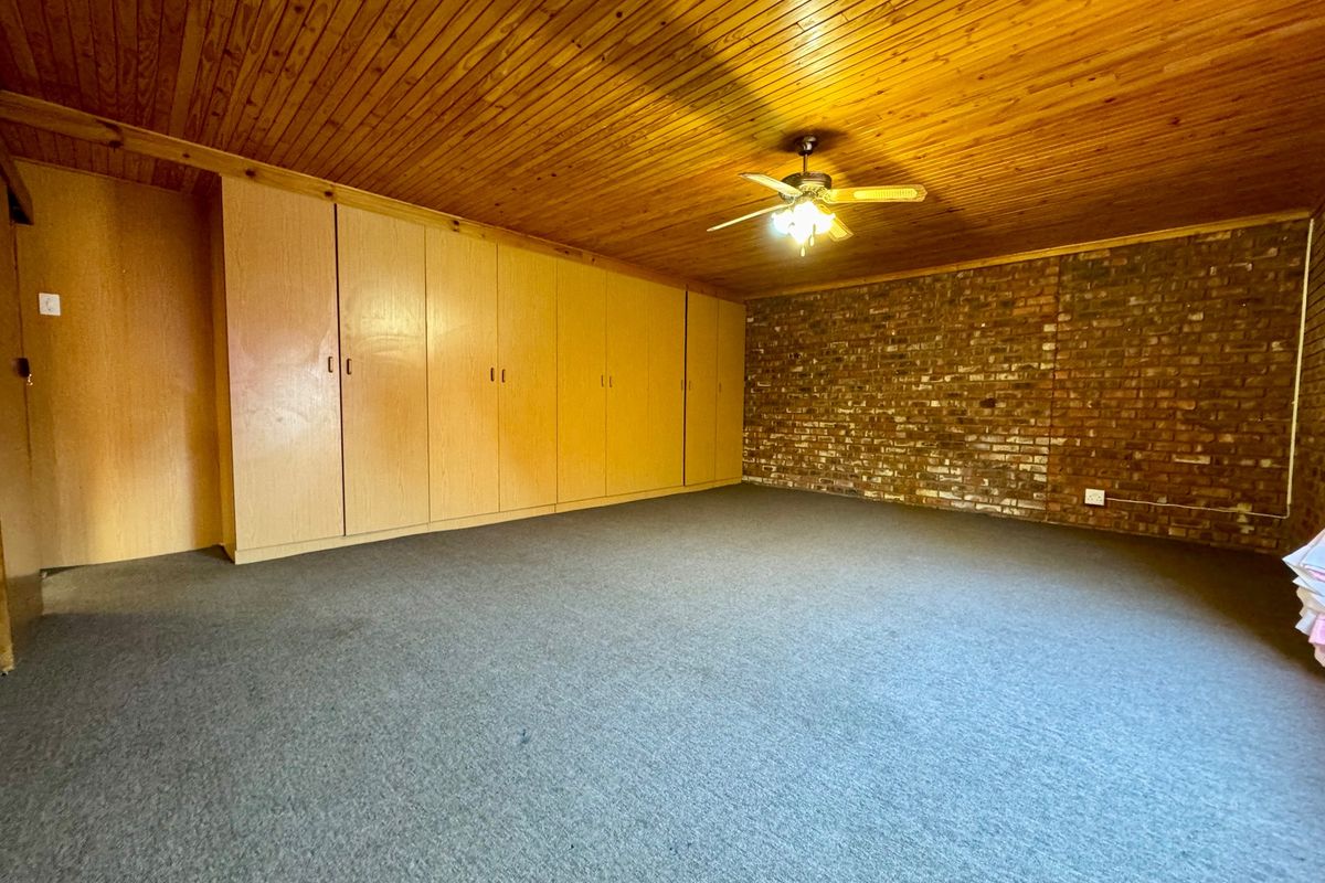 Spacious bedroom featuring extensive built-in cupboards, a rustic exposed brick feature wall, and a timber-clad ceiling with an integrated fan.