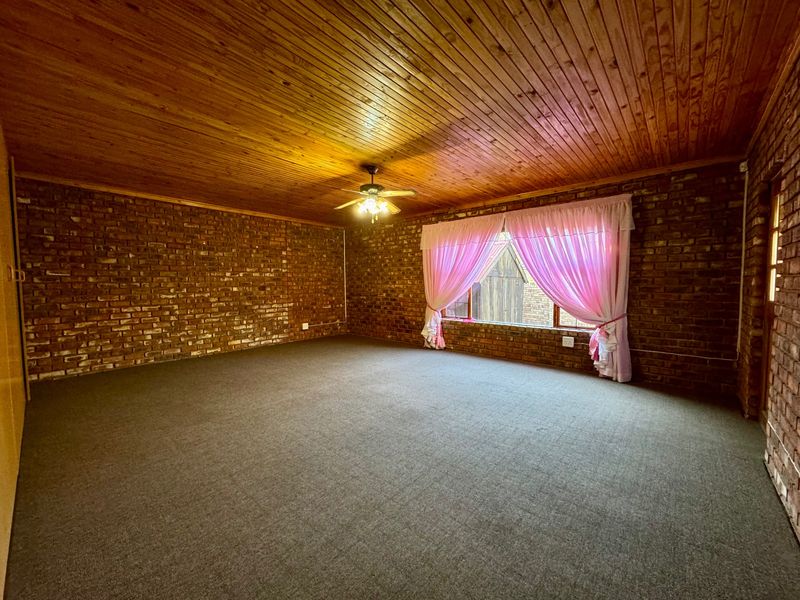 Spacious living area featuring rustic exposed brick walls, a warm timber ceiling, and a ceiling fan, offering a versatile blank canvas for interior design.