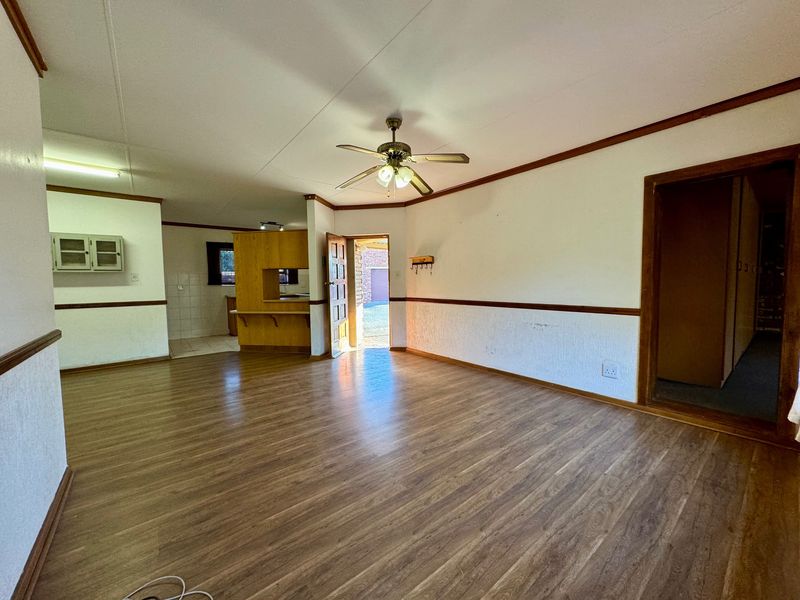 Spacious open-plan living area featuring laminate flooring, a ceiling fan, and a functional kitchen layout with a breakfast counter.