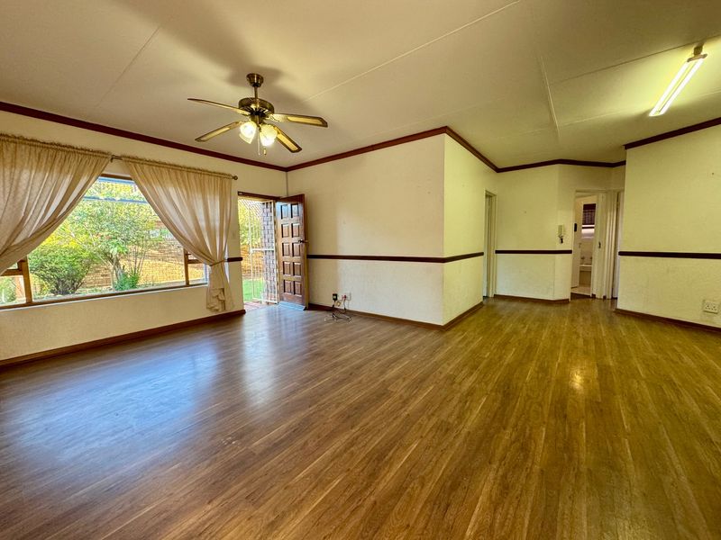 Spacious, empty living area featuring laminate flooring, a ceiling fan, and direct access to the garden through a security-fitted door.