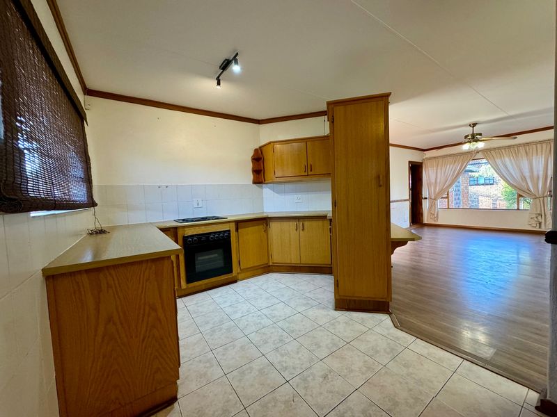 Open-plan kitchen and living area featuring dated wooden cabinetry, built-in oven, hob, and a combination of tiled and laminate flooring.