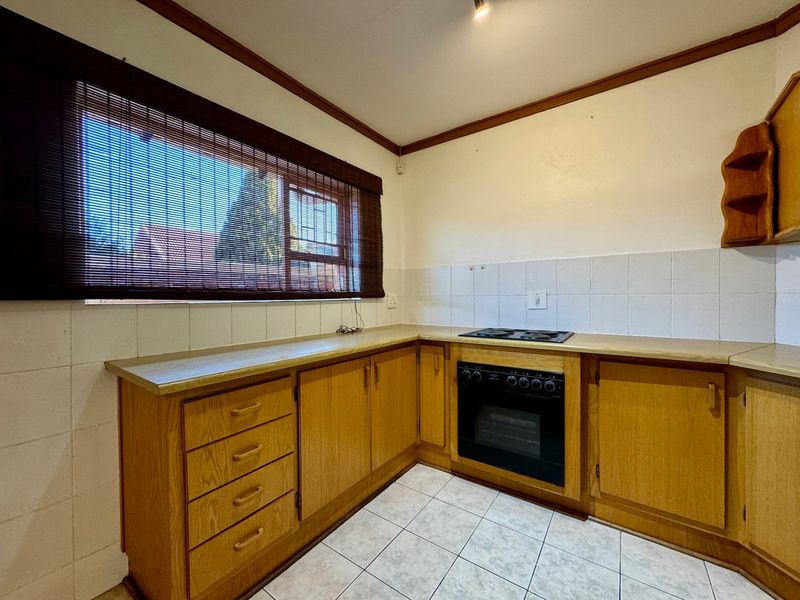 A functional kitchen featuring wooden cabinetry, built-in oven, electric hob, tiled splashback, and tiled flooring, offering a classic layout ready for modern updates.