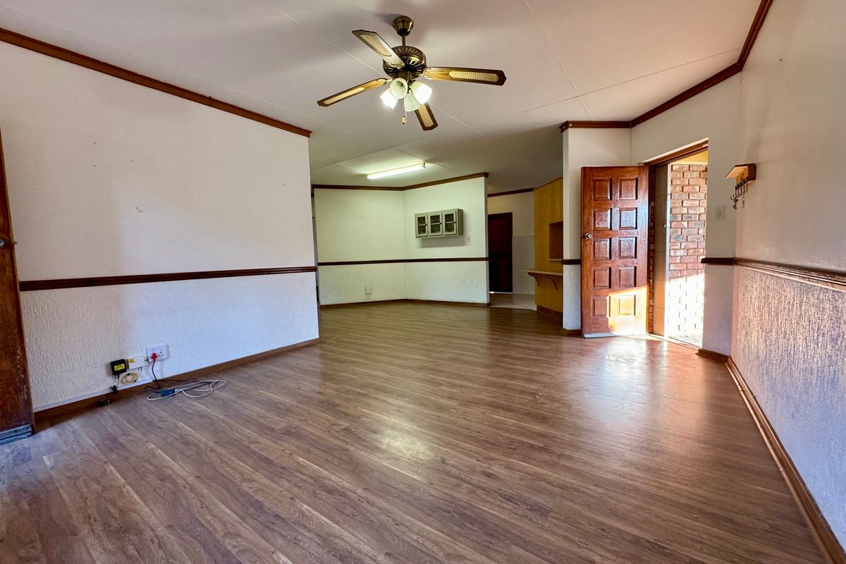 Spacious, empty living area featuring laminate flooring, a ceiling fan, and traditional chair rail molding, offering a blank canvas for renovation.