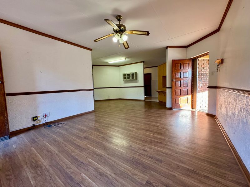 Spacious, empty living area featuring laminate flooring, a ceiling fan, and traditional chair rail molding, offering a blank canvas for renovation.