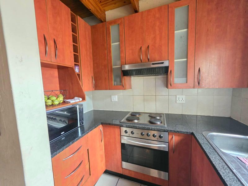 A functional kitchen featuring warm-toned cabinetry, granite countertops, integrated oven and hob, and exposed timber ceiling beams.