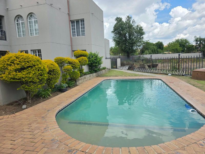Outdoor pool area featuring a swimming pool with brick paving, perimeter fencing, and established garden landscaping.
